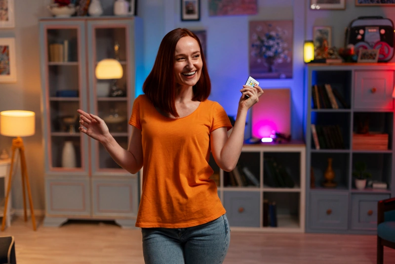 Mulher sorri enquanto liga sua iluminação inteligente com um controle remoto.